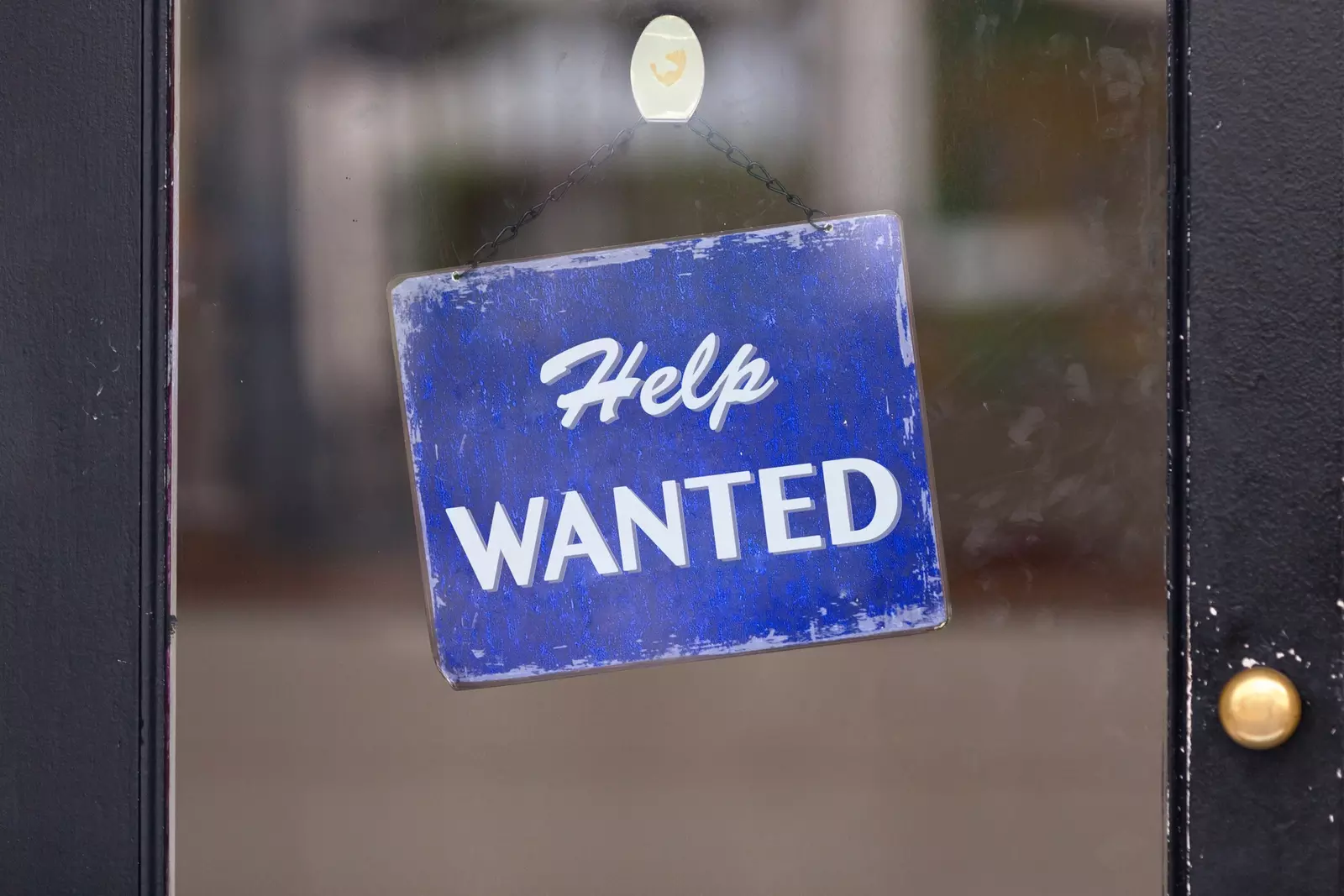 Help wanted sign hanging on glass door due to slow hiring recovery after COVID-19