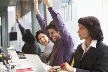 Excited employees sitting side by side at desks celebrating at a people-focused company