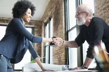 HR pro and executive standing in small office shaking hands after HR technology plan approval