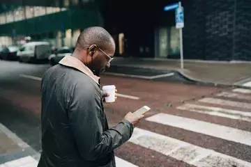 Remote worker checking payroll on mobile phone while walking in crosswalk
