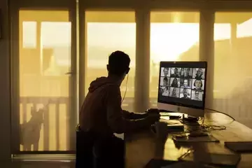 Remote worker on virtual meeting looking out window while sun sets